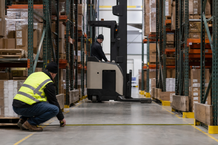 Warehouse planner measuring clear aisle width near a reach truck
